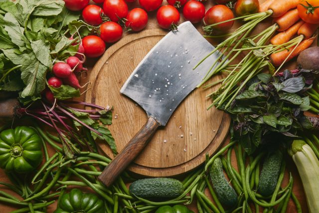 metal cleaver on cutting board with organic green and red vegetables