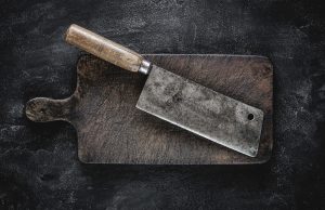 Why Do Meat Cleavers Have a Hole? rustic cutting board and meat cleaver on dark background