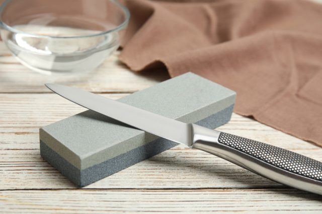 sharpening stone and knife on white wooden table